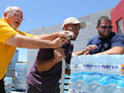 This Tuesday, June 14, 2016 photo Leo Block, left, Matari Phason, center, and Brian Juarez, right, push part of a shipment of 20,000 water bottles donated by Yellow Cab of Phoenix to Central Arizona Shelter Services, Arizona&#039;s largest homeless shelter, to help prepare for the summer heat in Phoenix, Ariz.