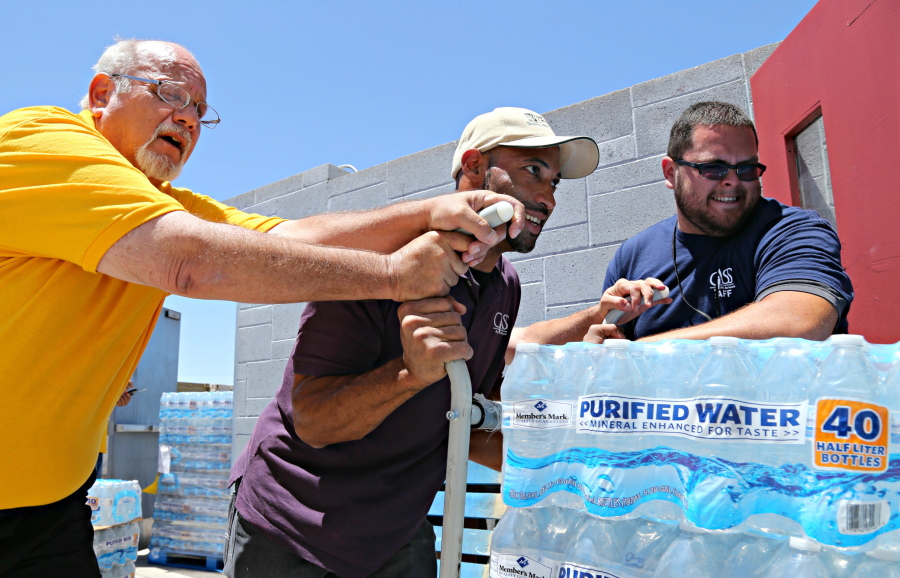 This Tuesday, June 14, 2016 photo Leo Block, left, Matari Phason, center, and Brian Juarez, right, push part of a shipment of 20,000 water bottles donated by Yellow Cab of Phoenix to Central Arizona Shelter Services, Arizona&#039;s largest homeless shelter, to help prepare for the summer heat in Phoenix, Ariz.