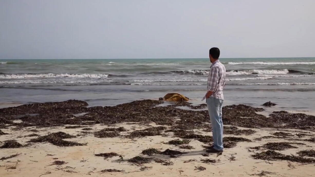 A man looks at a body, laying in the surf at center, Friday near Zwara, Libya. More than 100 bodies were pulled from the sea after a smuggling boat carrying mainly African migrants sank in the Mediterranean.