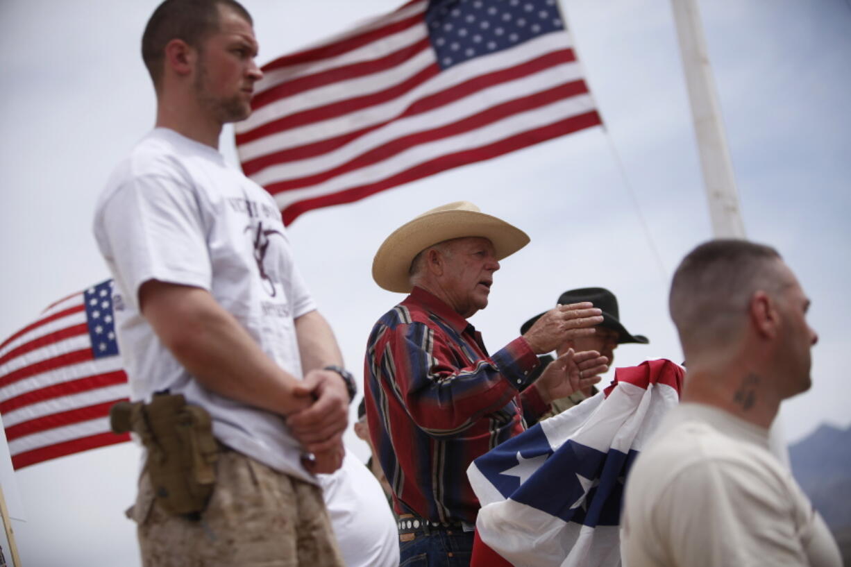 Rancher Cliven Bundy, flanked by armed supporters, speaks at a protest camp on April 18, 2014, near Bunkerville, Nev. Twelve of 19 defendants want separate trials in the federal criminal case involving the cattleman and an armed standoff near his southern Nevada ranch. The 70-year-old state sovereignty figure and three of his sons are among those whose attorneys have filed documents in recent weeks seeking to sever their cases from the rest.