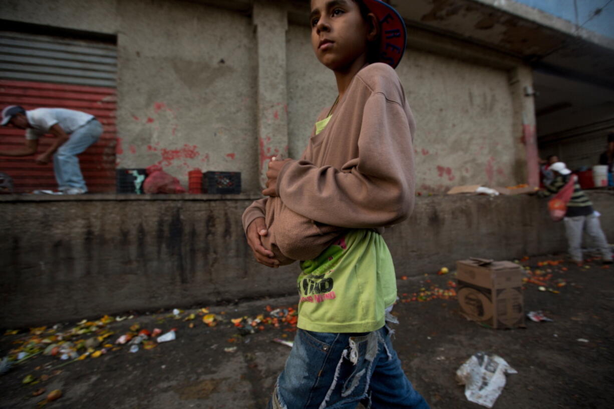 A boy carries two pineapples he found in the trash area of the Coche public market in Caracas, Venezuela. Staples such as corn flour and cooking oil are subsidized, costing pennies at the strongest of two official exchange rates. But fruit and vegetables have become an unaffordable luxury for many Venezuelan families.