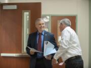 Clark County Councilor David Madore, left, is served with a summons by process server Brian Davis to appear at a deposition in connection with Oliver Orjiako's lawsuit against him, Tuesday morning at the Clark County Public Service Center in Vancouver.