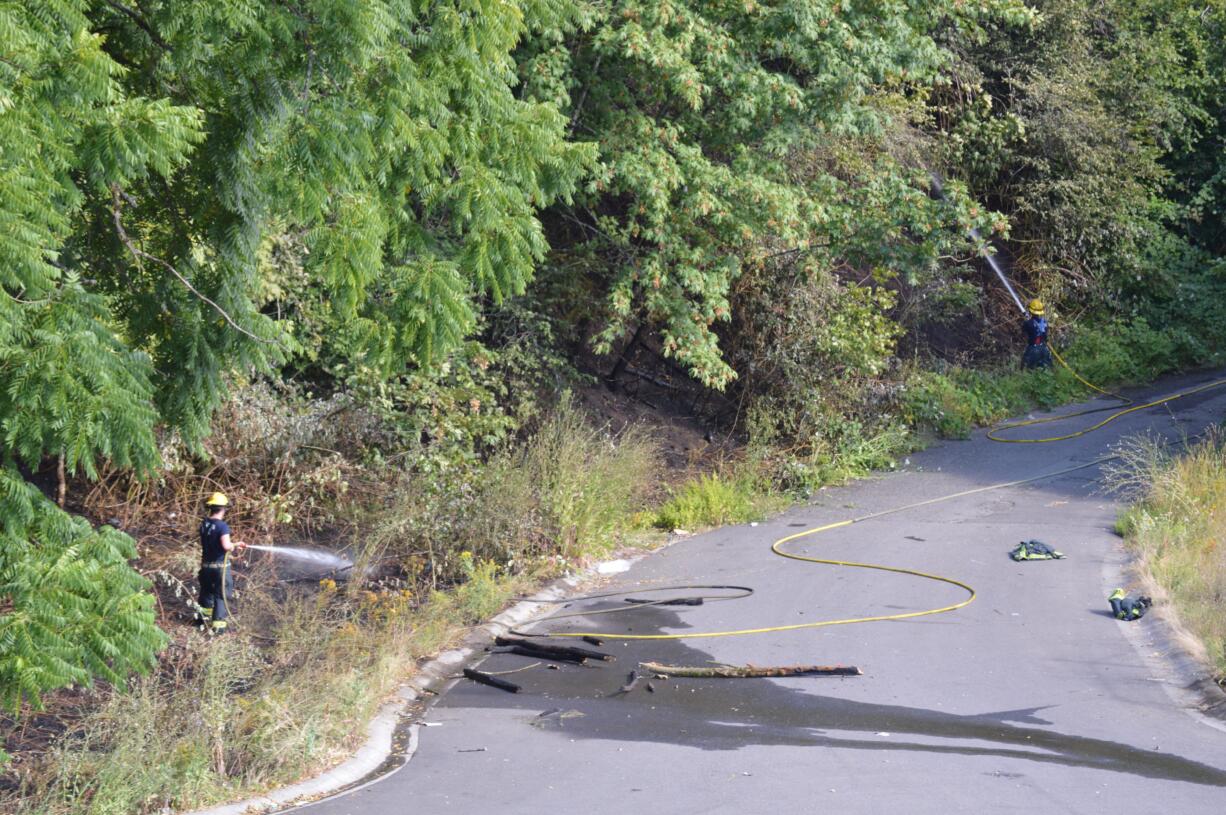 Vancouver firefighters work to cool off a brush fire Tuesday afternoon at the base of a hill by Olive Street in the Lincoln neighborhood.