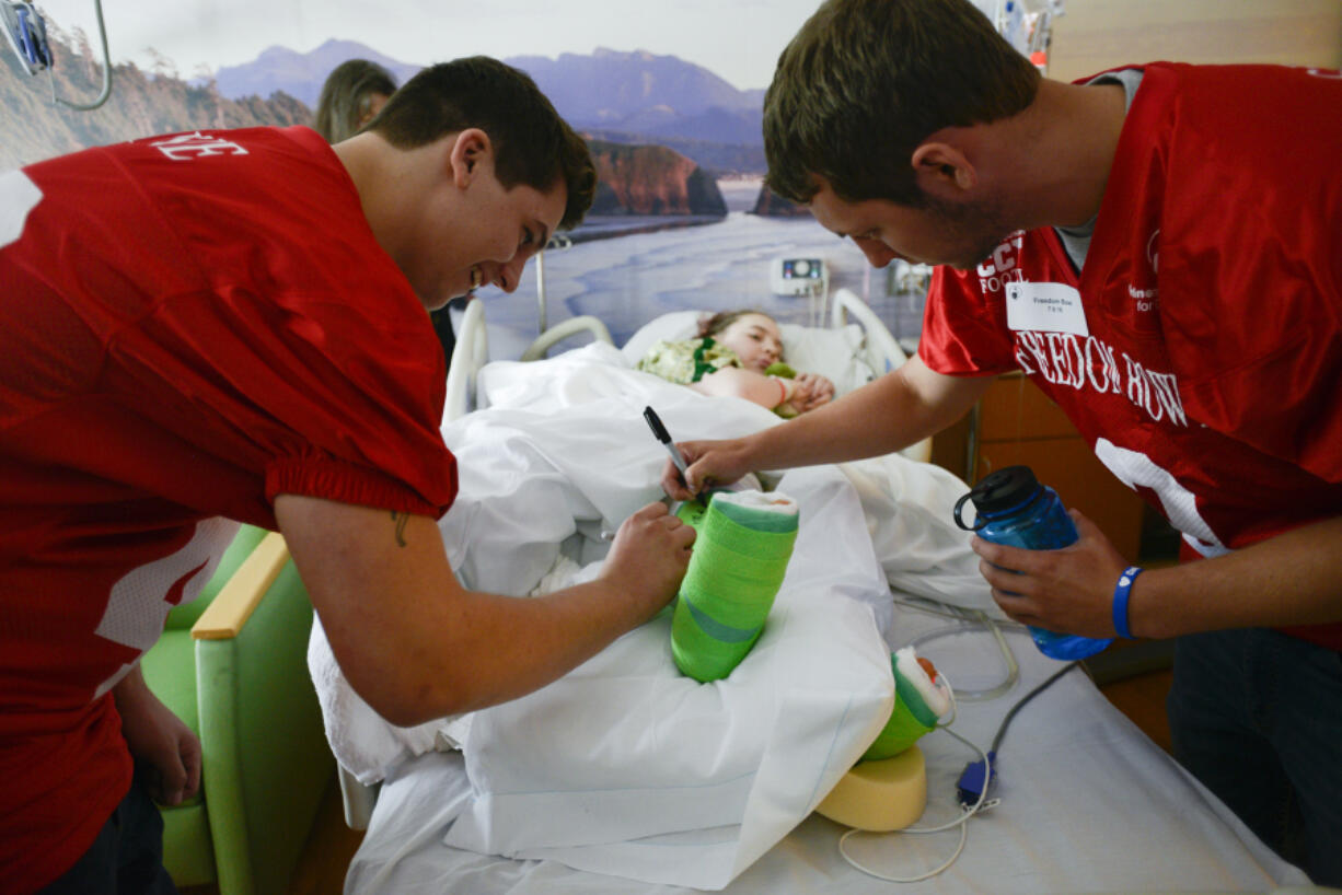 Stone Sabourin of Hudson's Bay High School, left, and Dalton Morgan of La Center High School, sign the cast of Shriner patient Julia Willis at Shriners Hospital in Portland.