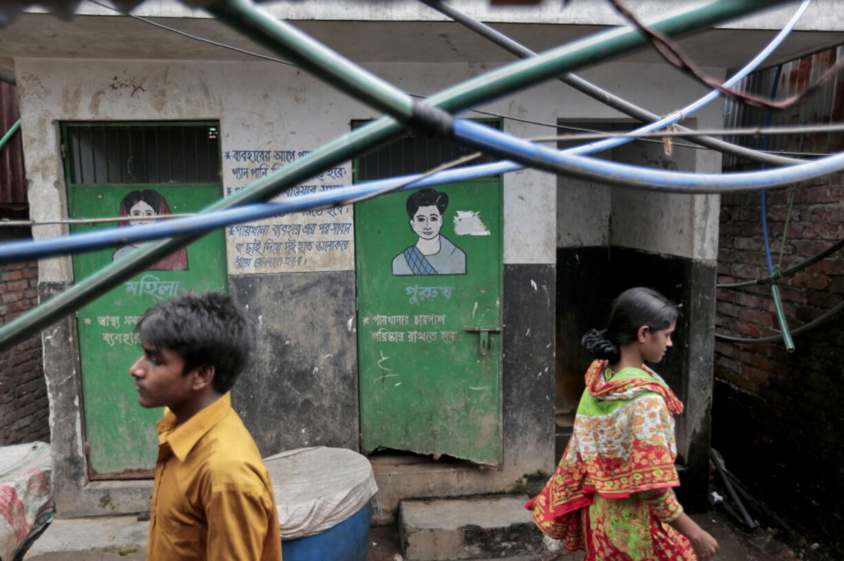 In this June 1, 2016 photo, Bangladeshis walk past a public toilet in a slum area in Dhaka, Bangladesh. Bangladesh&#039;s overpopulated urban areas are proving to be more of a challenge in the campaign for sanitation, mostly because the opportunity for contaminating water supply is much higher. (AP Photo/A.M.