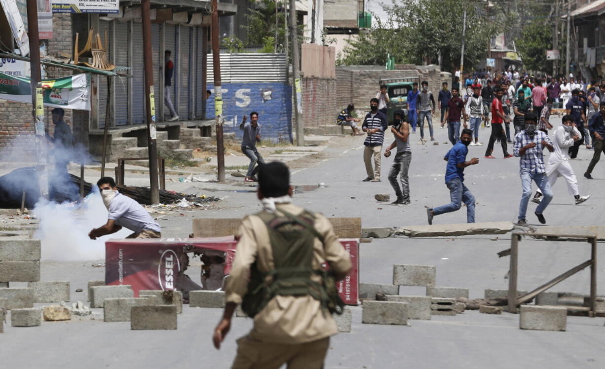 A masked Kashmiri protester prepares to throws a brick at an Indian policeman during a protest in Srinagar, Indian controlled Kashmir, Saturday, July 9, 2016. Indian authorities imposed an indefinite curfew in most parts of Kashmir on Saturday, a day after government forces killed the top rebel commander in the disputed Himalayan region, officials said, describing it as a major success against rebels fighting Indian rule.