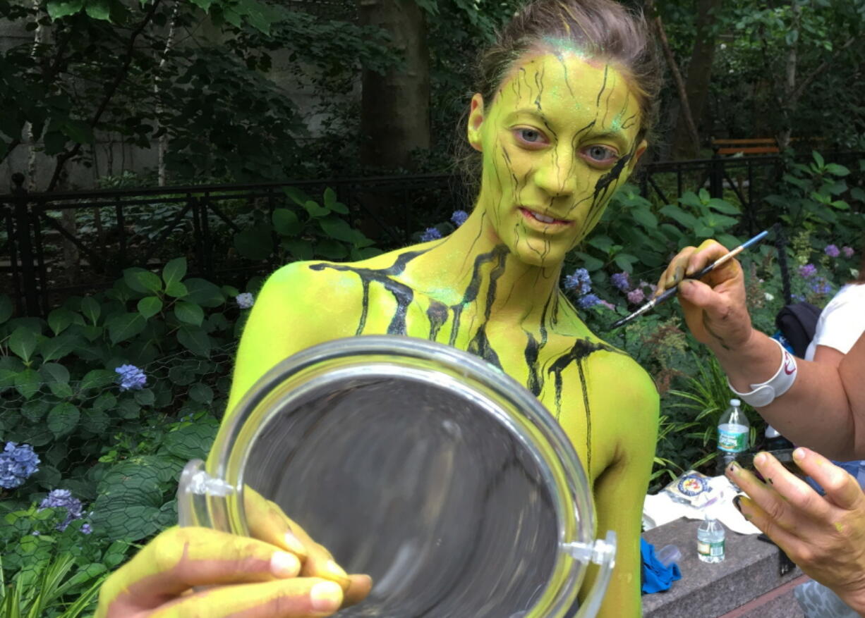 Megan Slawkawski looks at her reflection as bodypainter artist Uta Brauser applies paint Saturday at NYC Bodypainting Day in New York.