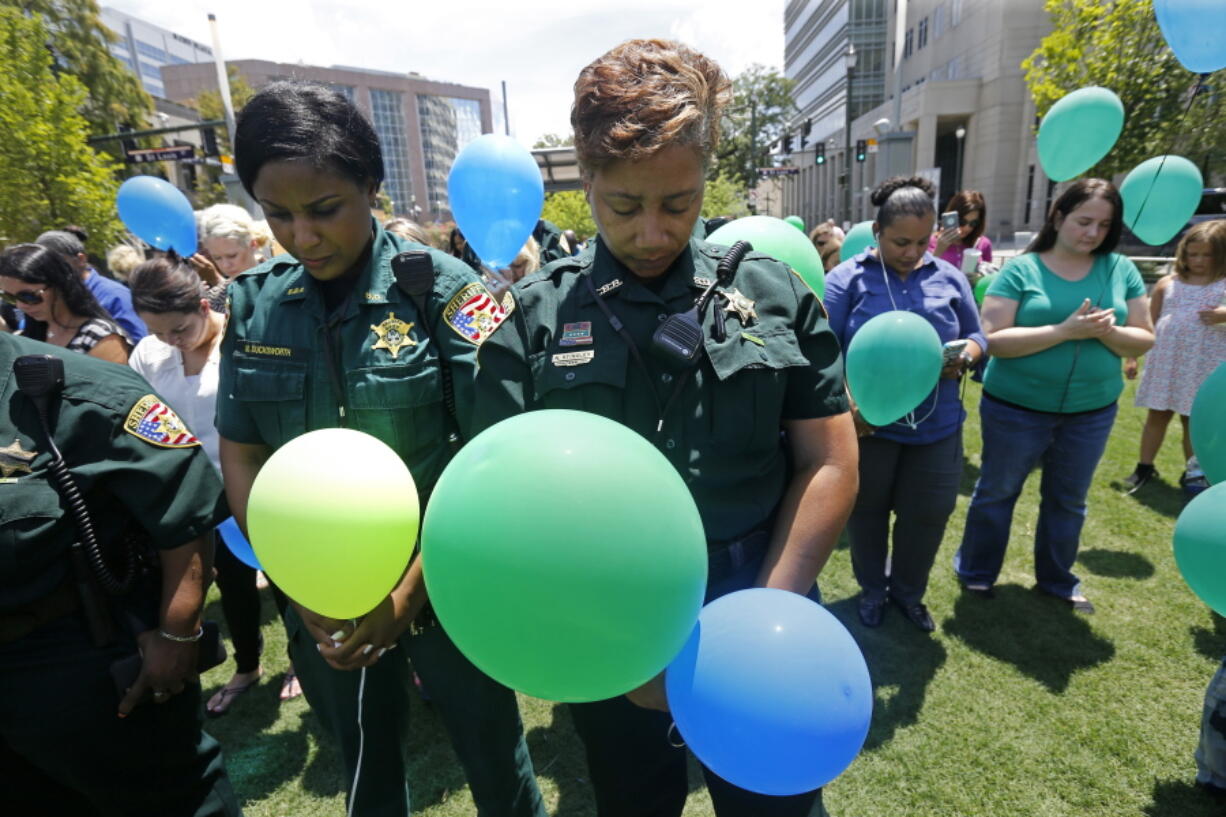 East Baton Rouge Sheriff&#039;s deputies Natasha Stingley, right, and Minnie Ducksworth bow their heads in prayer before releasing balloons at a noon vigil organized by municipal court workers in downtown Baton Rouge, La., Wednesday, July 20, 2016, in honor of recent slain and injured sheriff deputies and police.