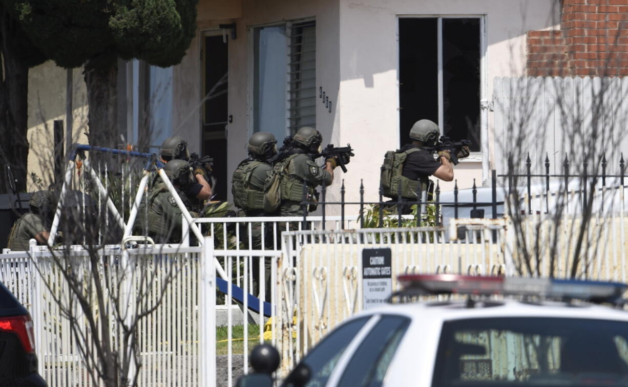 Heavily armed police officers surround a house Friday in San Diego, urging a man inside to surrender. They were searching for man described as a possible accomplice in a shooting Thursday night that left one officer dead.