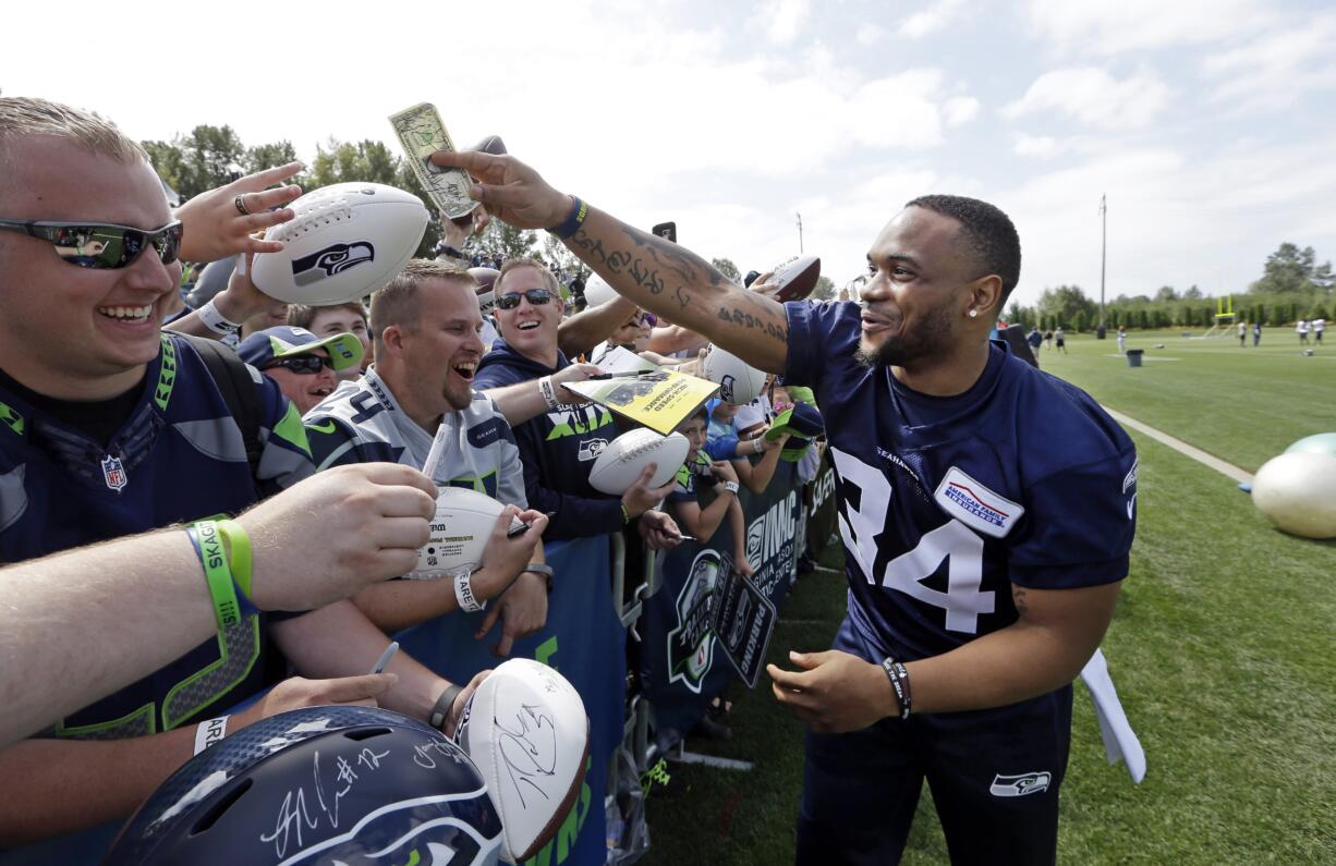 Seattle Seahawks' Thomas Rawls returns a dollar bill that he autographed after playfully threatening to keep it after the team's NFL football training camp Saturday, July 30, 2016, in Renton, Wash.