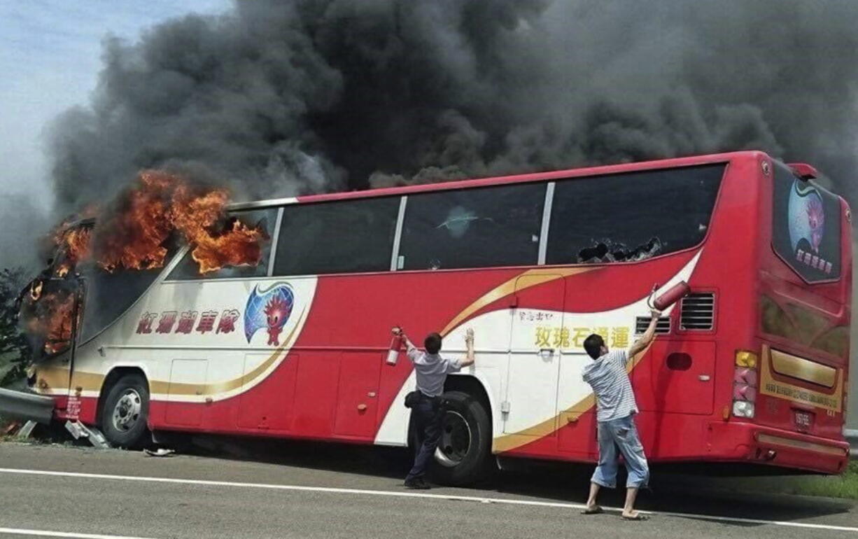 A policeman and another man try to break the windows of a burning tour bus Tuesday in Taoyuan, Taiwan.