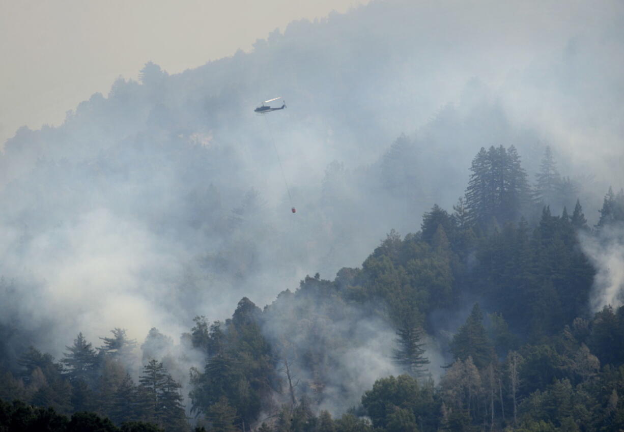 A helicopter flies in to make a water drop Saturday on a ridge above Rancho San Carlos in Carmel Valley, Calif.