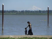 A woman and child walk along the edge of Vancouver Lake in June of last year. Later this month, volunteers will remove litter from the beach and nearby flushing channel.