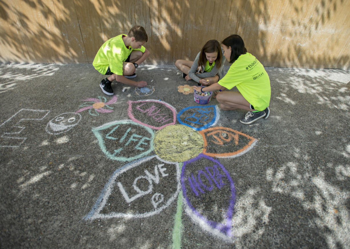 Thirteen-year-olds Clark Temme, from left, Alexandra Lafayette and Taryn Larsen, all members of The Joy Team, draw colorful flowers during Chalk the Walks on Tuesday morning along Main Street in Vancouver.