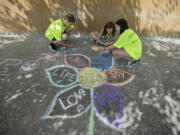 Thirteen-year-olds Clark Temme, from left, Alexandra Lafayette and Taryn Larsen, all members of The Joy Team, draw colorful flowers during Chalk the Walks on Tuesday morning along Main Street in Vancouver.