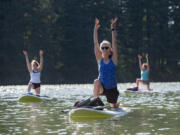 Washougal resident Susan Warford, front, joins fellow students as they try to do a low lunge on a paddleboard during a stand-up paddleboard yoga class on Round Lake in Camas.