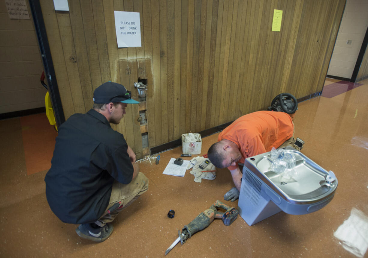 Ryan Romilly, in the orange T-shirt, and Jamie Wisenbaugh of Sarkinen Plumbing install a new fountain that provides filtered drinking water Monday at View Ridge Middle School in Ridgefield.