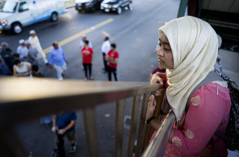 A young woman looks over the area from the steps of an elevated train station Saturday, Aug. 13, 2016, in the Queens borough of New York, near a crime scene after the leader of a New York City mosque and an associate were fatally shot as they left afternoon prayers. Police said 55-year-old Imam Maulama Akonjee and his 64-year-old associate, Tharam Uddin, were shot as they left the Al-Furqan Jame Masjid mosque.