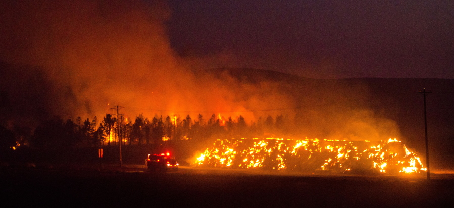 A fire truck moves along Hwy 125 past a blazing stack of hay bales north of Walla Walla during a large wildfire Sunday night. Firefighters from several districts were able to stop the blaze at Hwy 125. The fire, whose cause in under investigation, burned about 15,000 acres in very high winds and was contained about 11:00p.