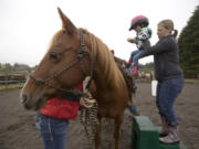 Allison Wilson helps Karleigh Anderson, 3, onto a horse as they take part in a session at the Rockin&#039; Hope Youth Ranch on the Villines family farm in La Center.