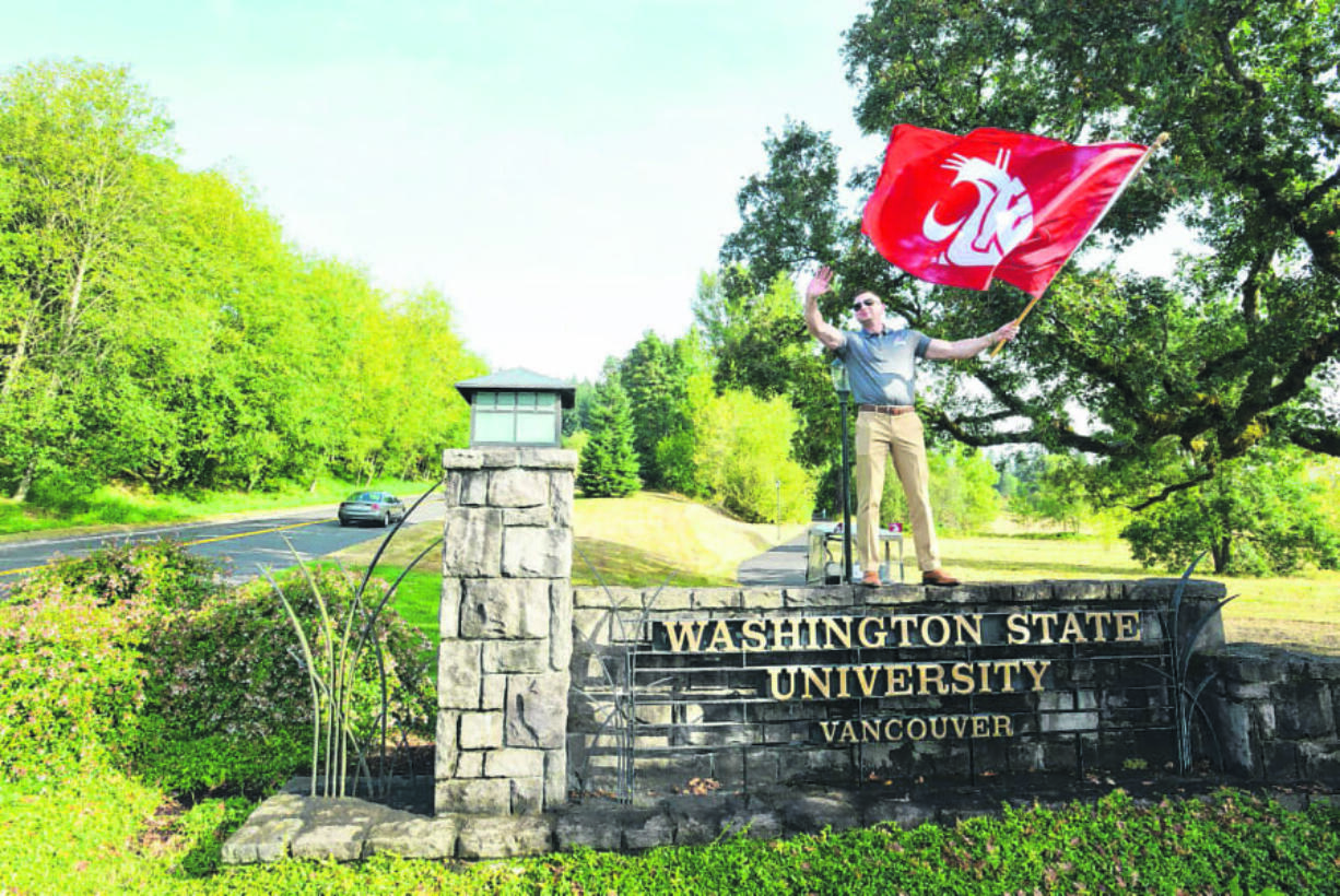 Max Ault, Director of Business Growth and Development for the Columbia River Economic Development Council, stands on top the Washington State University Vancouver sign at the campus entrance to greet students as they arrive on Aug. 22.