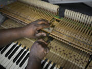 Leal Sylvester, a 1997 graduate and now the new director of instruction intern at the Piano Hospital in Vancouver, works on adjusting the hammer blow distance on a piano.