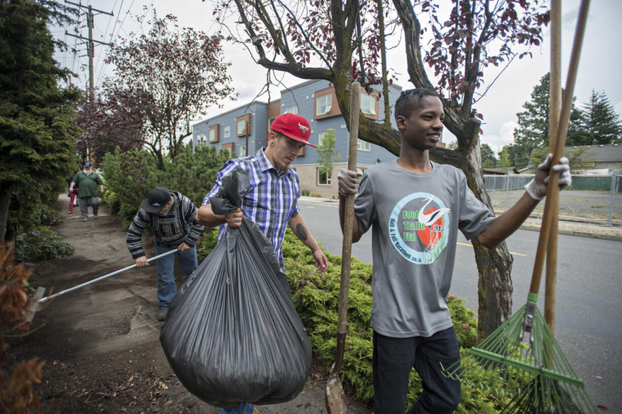 Share House resident Ivan Hand, center, clears leaves and debris during a neighborhood cleanup with fellow resident Nelson Powell, right, on Thursday afternoon.