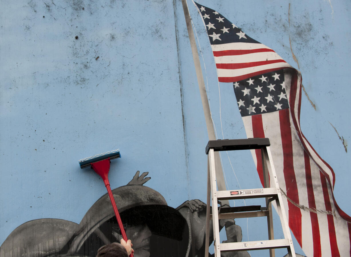 Volunteers scrub mold and moss Wednesday from murals illustrating events during World War II on Vancouver&#039;s Remembrance Wall, just south of City Hall.