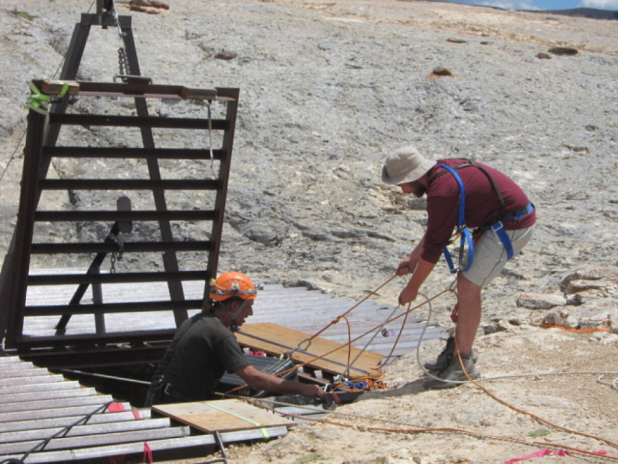 The U.S. Bureau of Land Management shows caving volunteer Juan Laden, left, taking supplies from an unidentified man to researchers at the bottom of Natural Trap Cave in northern Wyoming on July 13, 2016. A third consecutive season of excavations in the cave uncovered wolf, bison, lion and cheetah bones from around 12,000 years ago. (Gretchen Hurley/U.S.