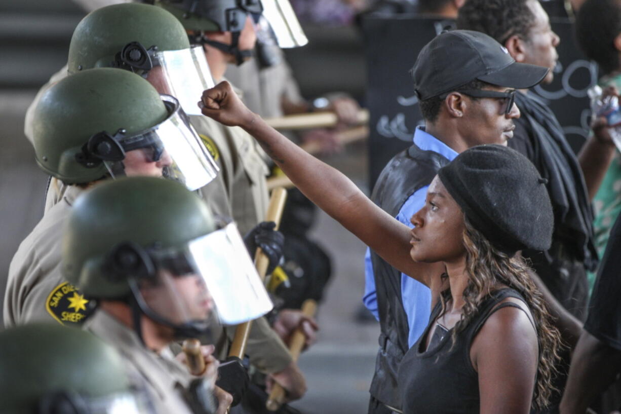 Ebonay Lee holds up her fist toward a line of sheriff&#039;s deputies as she and other people protest Wednesday in the San Diego suburb of El Cajon, Calif.