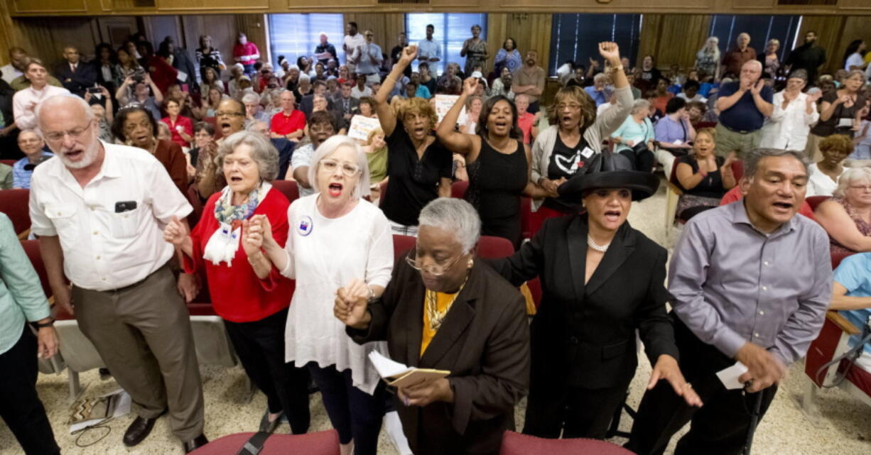 People rise and begin singing during the Guilford County Board of Elections meeting at the Old Guilford County Courthouse in Greensboro, N.C. The swing state of North Carolina could be pushed in a Republican or Democratic direction when the GOP-led State Board of Elections meets Thursday to finalize early voting plans for a third of the state&#039;s counties.