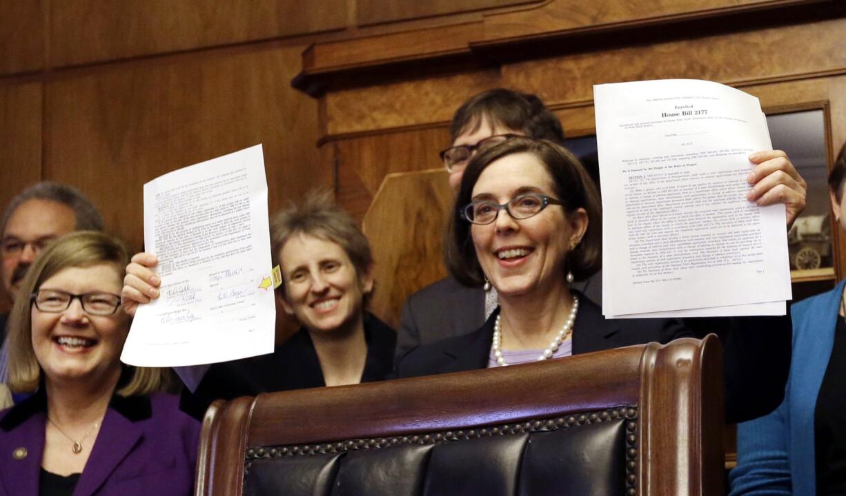 Oregon Gov. Kate Brown holds up an automatic voter registration bill after signing it March 16, 2015 in Salem, Ore. Oregon's new 'motor voter' program is fueling a surge in newly registered voters in the state under a new law that automatically registers anyone who gets or renews a driver's license. The Oregon Secretary of State's office said Tuesday that nearly 300,000 people have registered in the past 12 months and more than 75 percent of them those did so under the new law that took effect in January, 2016.