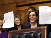 Oregon Gov. Kate Brown holds up an automatic voter registration bill after signing it March 16, 2015 in Salem, Ore. Oregon's new 'motor voter' program is fueling a surge in newly registered voters in the state under a new law that automatically registers anyone who gets or renews a driver's license. The Oregon Secretary of State's office said Tuesday that nearly 300,000 people have registered in the past 12 months and more than 75 percent of them those did so under the new law that took effect in January, 2016.