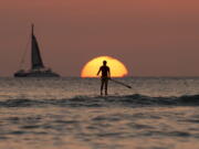 A paddleboarder looks our over the Pacific Ocean as the sun sets off of Waikiki Beach in Honolulu.