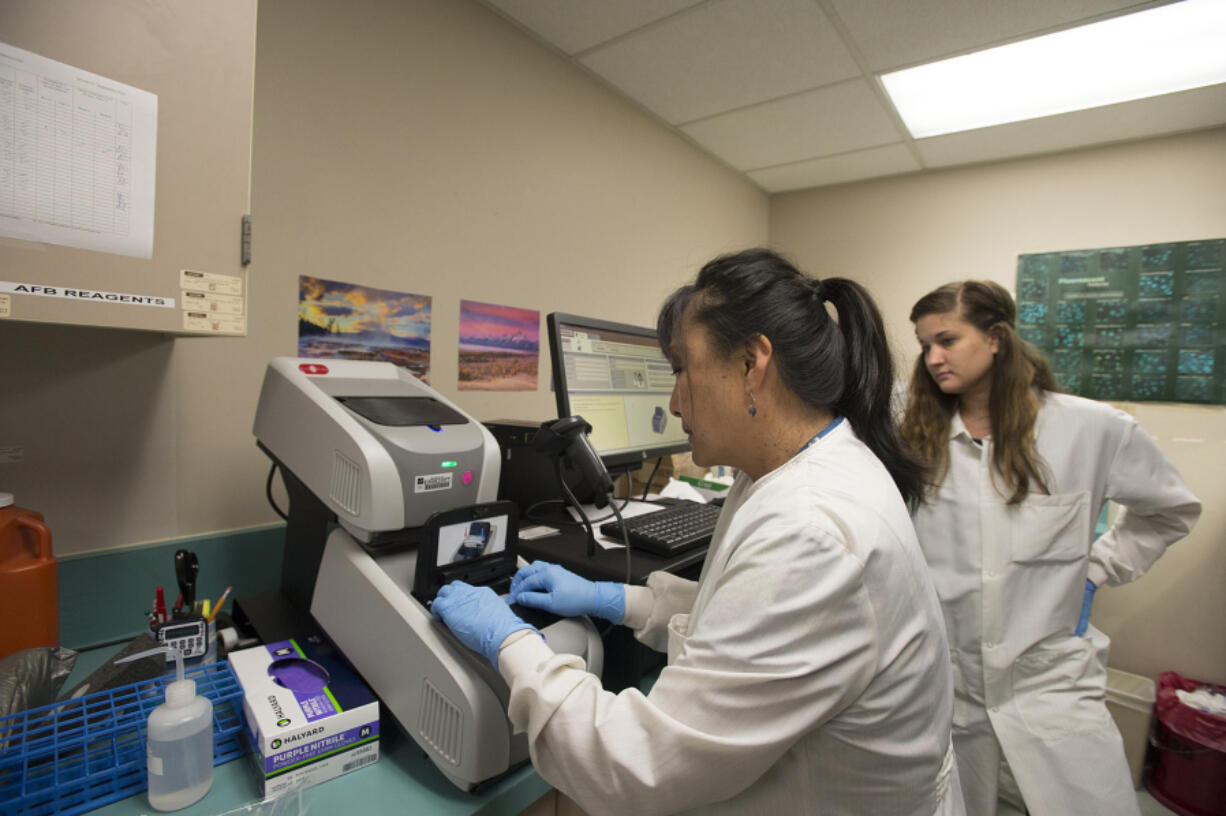 Microbiologist Lillian McLitus, left, inserts a sample into the new DNA testing machine at PeaceHealth Southwest Medical Center as Lue Ann MacKenzie, an Oregon Health &amp; Science University lab student, looks on. The new device can identify bacteria causing sepsis within an hour.