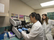 Microbiologist Lillian McLitus, left, inserts a sample into the new DNA testing machine at PeaceHealth Southwest Medical Center as Lue Ann MacKenzie, an Oregon Health &amp; Science University lab student, looks on. The new device can identify bacteria causing sepsis within an hour.