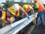 Washington State Department of Transportation maintenance worker Eustacio Valencia, left, tightens the bolts holding together a new  and old sections of guardrail along state Highway 500.