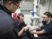 Central Vancouver: Petty Officer 2nd Class Evan Fitch, center, of Vancouver teaches blood-drawing techniques to Petty Officer 3rd Class Martin Salinas, left, while aboard the USS Bonhomme Richard, which is operating in the South China Sea.