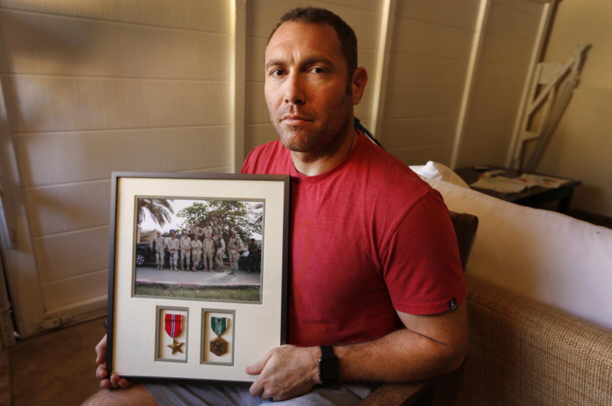 Robert D&#039;Andrea, a retired Army major and Iraq war veteran, holds a frame with a photo of his team on his first deployment to Iraq in his home in Los Angeles.