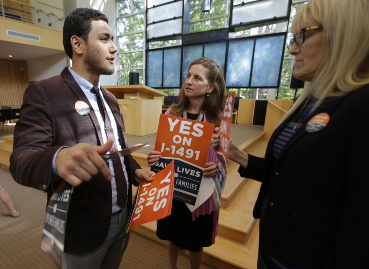 Dujie Tahat, left, hands out posters Sept. 21 to Marilyn Balcerak, right, and Rep. Tana Senn, D-Mercer Island, center, before a news conference in Bellevue, promoting Initiative 1491, which will be on the ballot in the November elections. (Ted S.