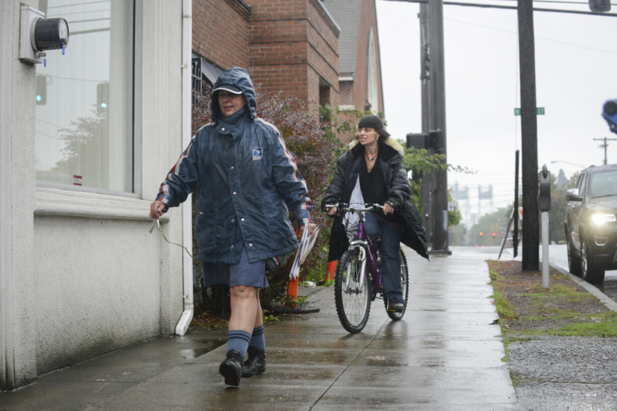 Mary Siebert, left, delivers mail to the Clark County Veterans Assistance Center in Vancouver in the rain on Oct. 13.