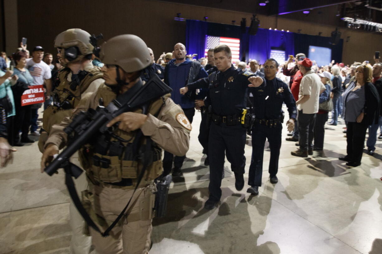 A man, at background center with blue sweater, is escorted by law enforcement officers moments after Republican presidential candidate Donald Trump was rushed offstage by Secret Service agents during a campaign rally in Reno, Nev., on Saturday, Nov. 5, 2016.