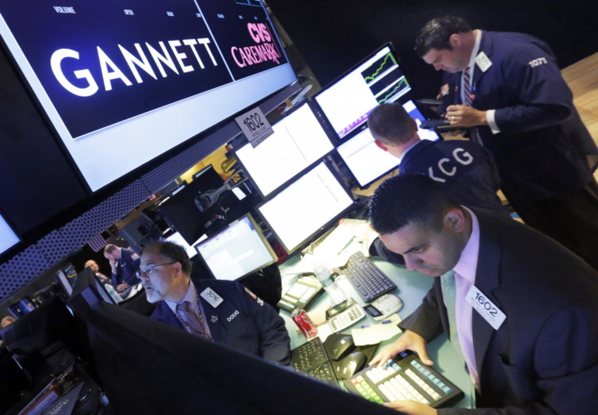 Specialist Michael Cacace, foreground right, works at the post that handles Gannett on the floor of the New York Stock Exchange. USA Today publisher Gannett, suffering from the ongoing print-ad declines that have hurt the broader newspaper industry, is cutting jobs as it reported a loss in its latest quarter, the company announced Thursday.