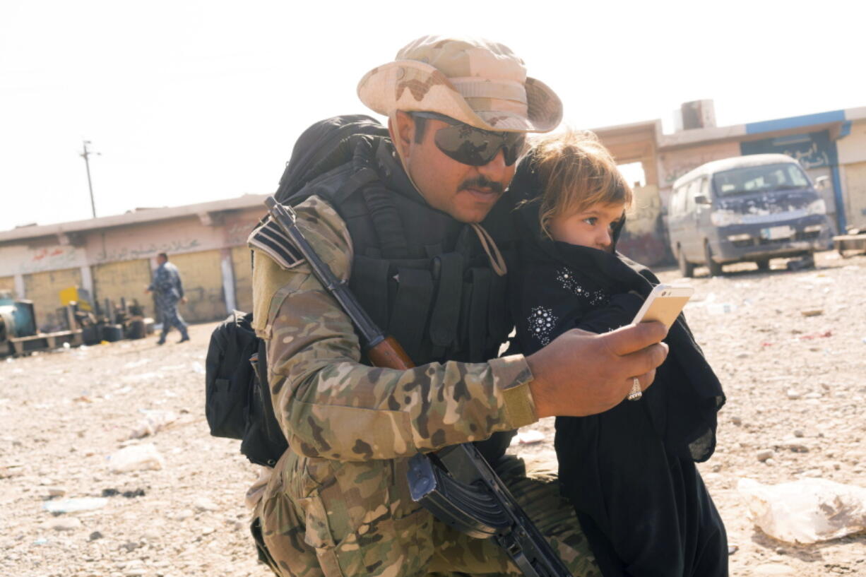 An Iraqi Soldier takes a selfie with the daughter of a man who identified himself as Omar Danoun at a collection point for people displaced by fighting in Mosul, in Gogjali, Iraq. Danoun, was later taken into custody by this and other soldiers during his interview with Associated Press. The soldiers believed he was with the Islamic State group and that he seemed to speak with a Syrian accent instead of an Iraqi accent.