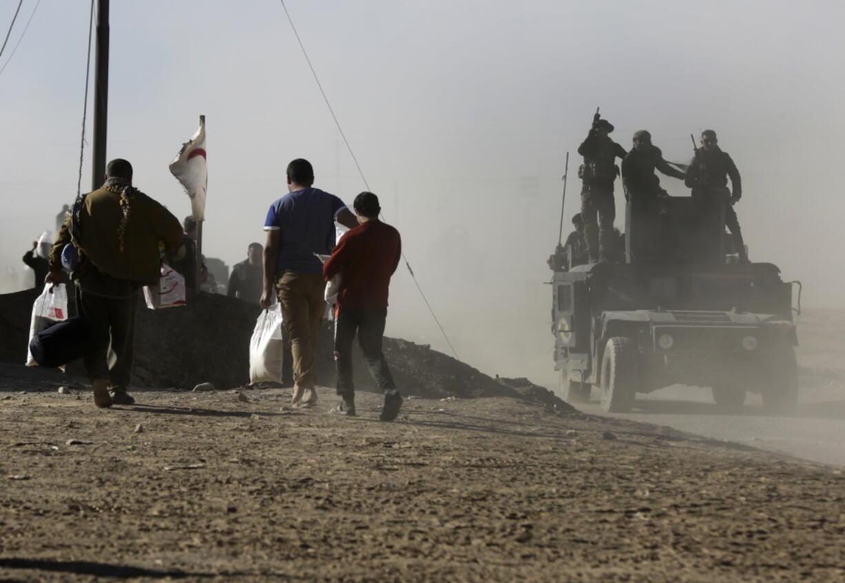 Iraqi soldiers stand atop their humvee as they pass civilians carrying food aid Wednesday in the Al-Samah neighborhood of Mosul, Iraq, on the front lines of the fighting.