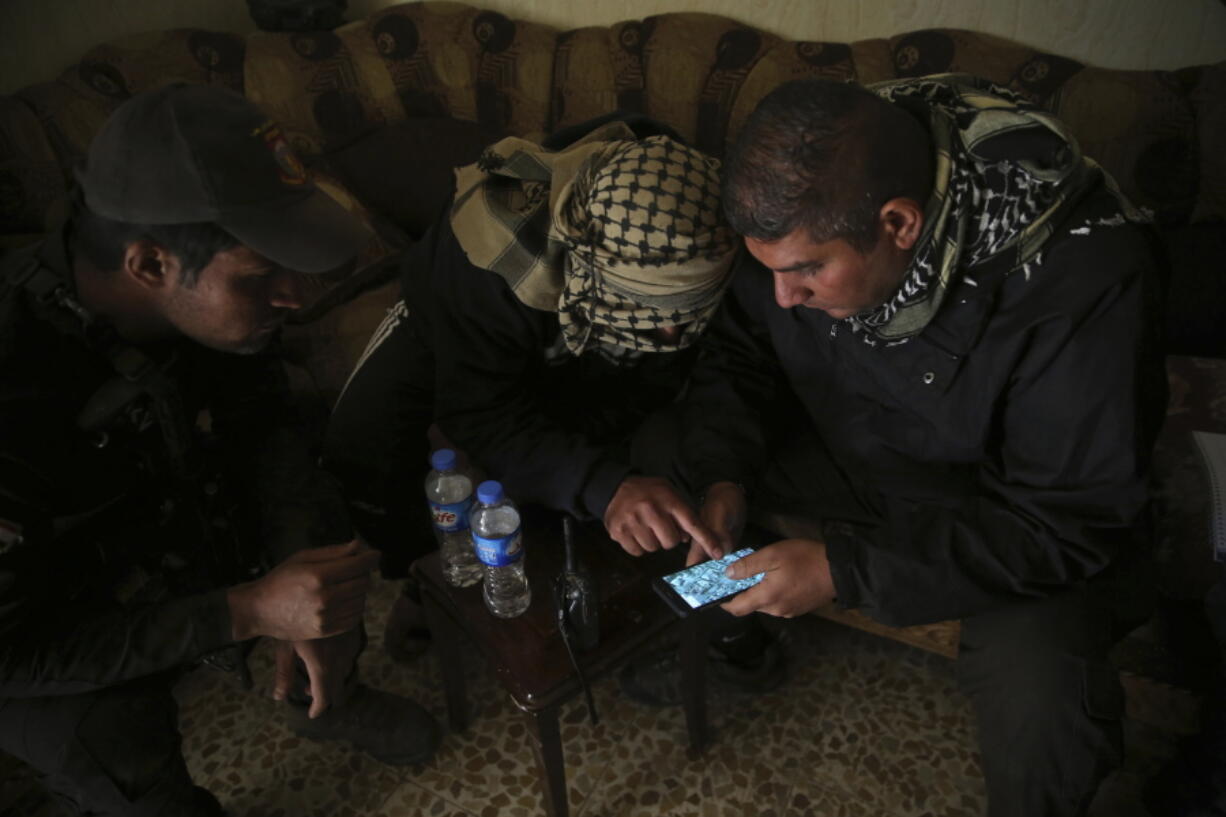 Special forces Lt. Col. Ali Hussein, right, listens to an Iraqi informant, center, giving information about Islamic State militant positions on a mobile map, in the Bakr front line neighborhood, in Mosul, Iraq, Friday Nov. 25, 2016. Iraqi special forces fought house to house in Mosul, while focusing efforts on winning hearts and minds among civilians and gleaning information about Islamic State militants holed up in buildings sometimes just a block away.