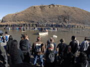 Dakota Access Pipeline protesters stand in the foreground and in the waist-deep water of the Cantapeta Creek, northeast of the Oceti Sakowin Camp, near Cannon Ball, N.D., on Wednesday. Officers in riot gear clashed again Wednesday with protesters near the Dakota Access pipeline, hitting dozens with pepper spray as they waded through waist-deep water in an attempt to reach property owned by the pipeline&#039;s developer.