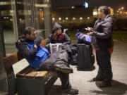 Housing case manager, Jamie Spinelli, right, asks Anthony Bordelon and Mandy Seitz what items they need to keep warm Dec. 17 outside the Vancouver Community Library. Volunteers with the nonprofit organization Food with Friends hand out food and other items to the homeless Saturday nights in downtown Vancouver.