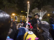 Rabbi Shmulik Greenberg holds a torch to light a menorah Monday evening at a Hanukkah celebration for the community in Esther Short Park in Vancouver. Rabbi Greenberg asked the children to join him in singing a song and holding the torch.