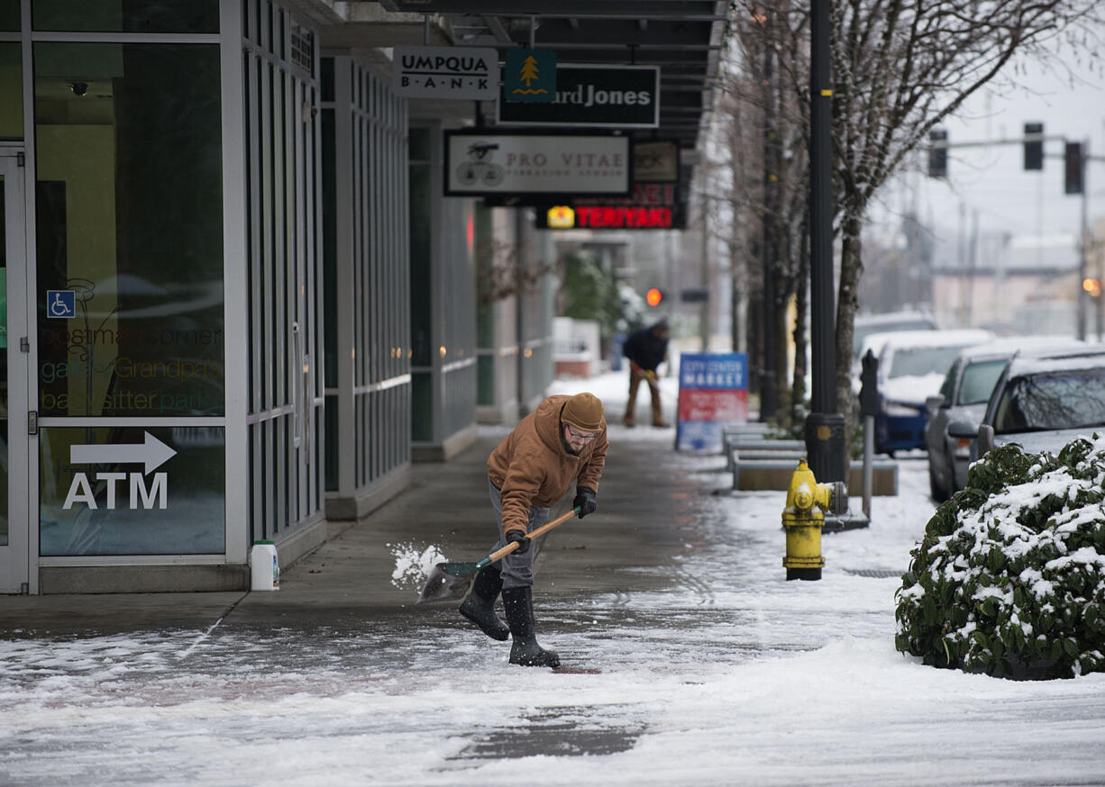 Jerrad Isch of Vancouver shovels ice and snow to clear a pathway to Umpqua Bank for customers in downtown Vancouver on Jan. 4. Local road crews are preparing to take to the streets Monday morning should the threat of snow hold true.